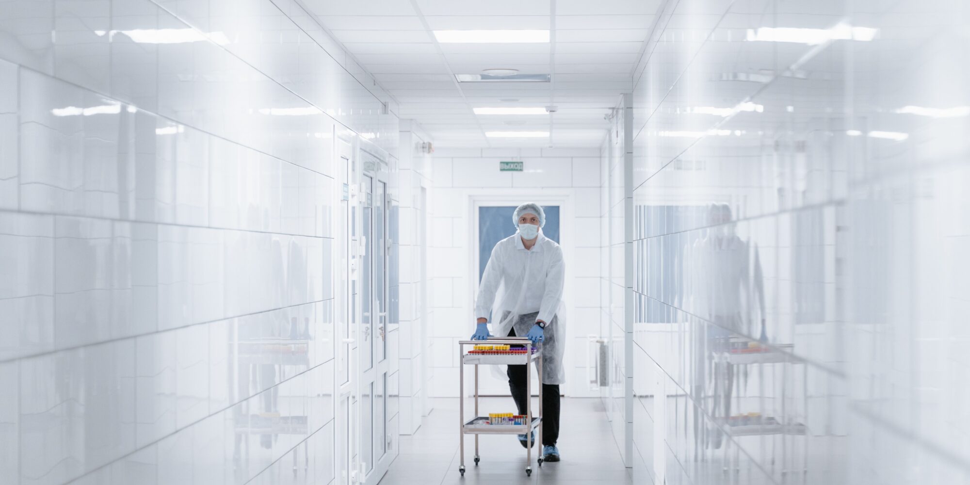Personal i full skyddsutrustning kör en vagn i en steril, kaklad korridor med ett fogfritt och hygieniskt golv.
