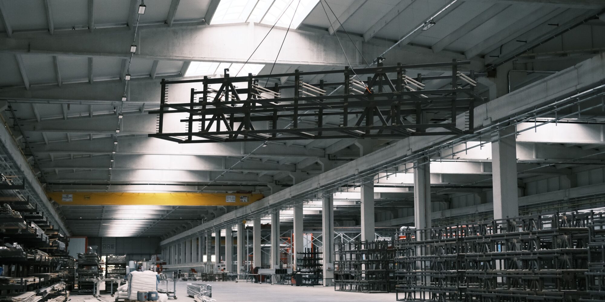 Ett stort industrigolv i en produktionshall med traverskran och tunga ställage, där proaktivt underhåll minskar reparationskostnader.