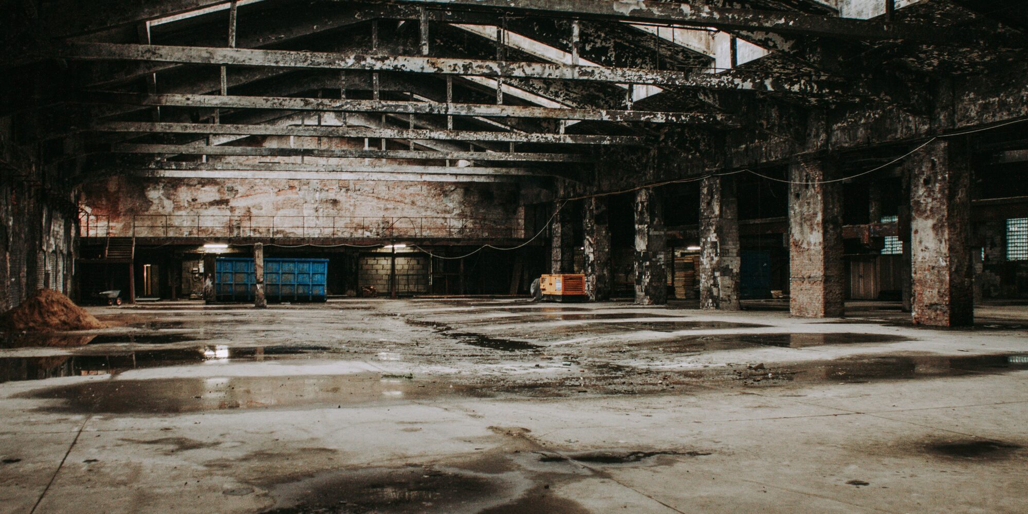 Ett slitet, fläckigt och skadat betonggolv i en stor industrihall innan en strategisk golvrenovering och diamantslipning.
