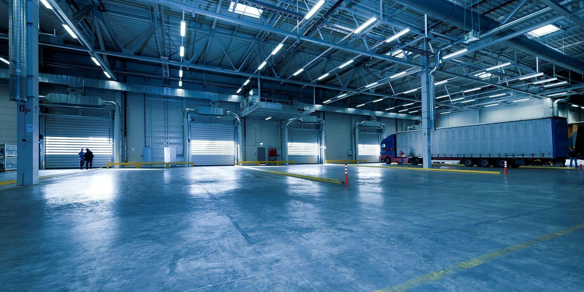 Ett rent och polerat betonggolv i en modern industrilokal med lastbilsportar där dagsljuset strömmar in.
