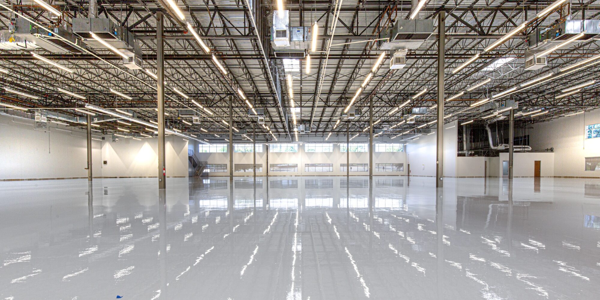 Polerat och reflekterande betonggolv i en stor, ljus industrilokal som speglar takbelysningen.